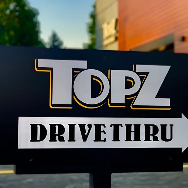 Black Topz Drive-Thru sign with a white arrow pointing right, in front of a restaurant.