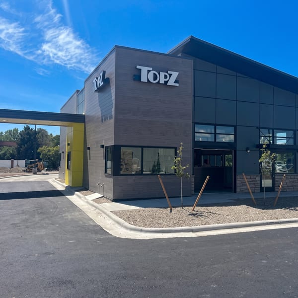 Modern TopZ restaurant exterior with a drive-thru lane, dark siding, and large windows under a blue sky.