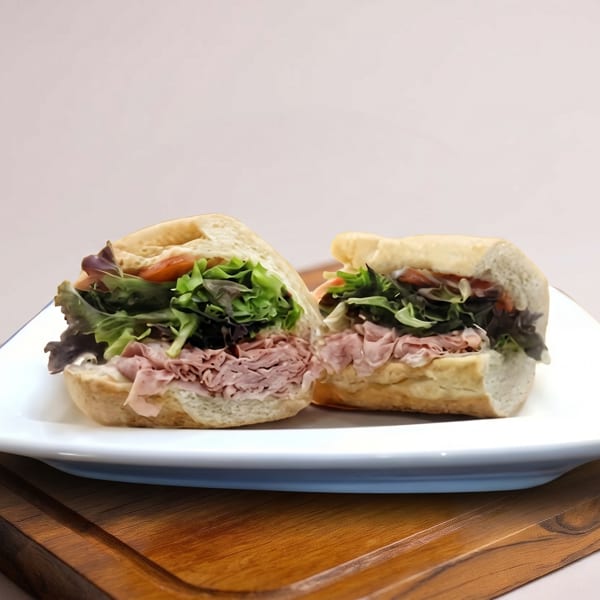 Two halves of a sandwich with meat and lettuce on a white plate over a wooden board.