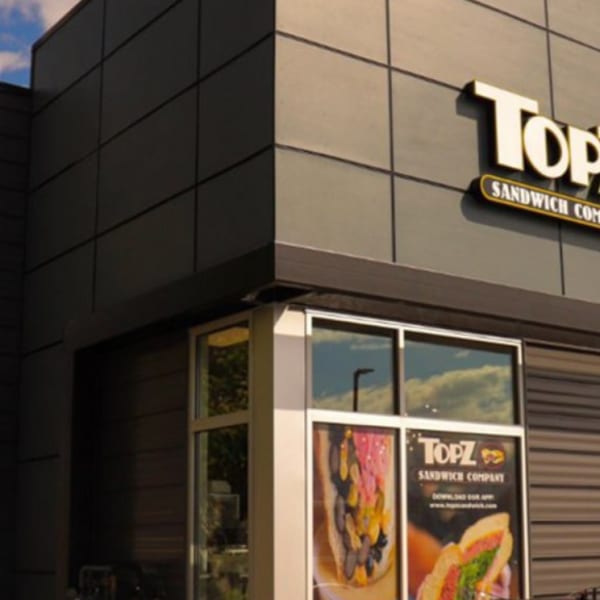 Topz Sandwich Company building exterior with a prominent sign, dark gray facade, and large windows.